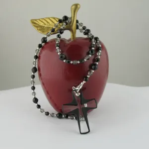 Ett glänsande rött äpple med ett guldblad sitter på en vit yta. En tråd av Silverpärlor runda blanka 2mm/0,9mm pärlor är draperad runt äpplet.
