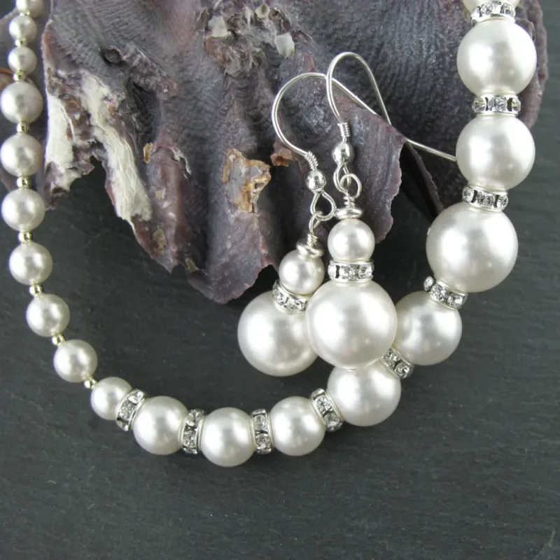 Närbild av Silverpärlor runda blanka 2mm/0,9mm som används i ett pärlhalsband och matchande örhängen med strassdistanser, på en mörk skifferbakgrund bredvid en texturerad snäcka.