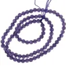 En spiralformad sträng av runda, genomskinliga lila pärlor som är sammanfogade med lila tråd och arrangerade i en spiralform mot en vit bakgrund.
