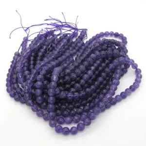 Flera trådar med runda, glänsande lila pärlor är grupperade tillsammans, varje tråd hålls av en ljuslila tråd med lösa ändar som syns upptill. Pärlorna är arrangerade i en lätt trasslig hög på en vit yta.