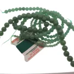 Aventurin grön rund ädelsten 4-6mm pärlor är arrangerade på ett grönt gängat kort märkt "For stringing pearls and beads", mot en vit bakgrund.