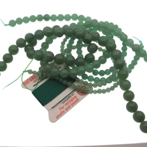 Aventurin grön rund ädelsten 4-6mm pärlor är arrangerade på ett grönt gängat kort märkt "For stringing pearls and beads", mot en vit bakgrund.