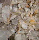 Närbild på Bergkristall rund ädelsten 4-6mm, med grova, opolerade klara kvartskristaller med gulaktiga och brunaktiga mineralfläckar i olika storlekar och oregelbundna former grupperade tillsammans.