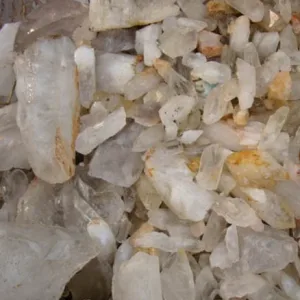 Närbild på Bergkristall rund ädelsten 4-6mm, med grova, opolerade klara kvartskristaller med gulaktiga och brunaktiga mineralfläckar i olika storlekar och oregelbundna former grupperade tillsammans.