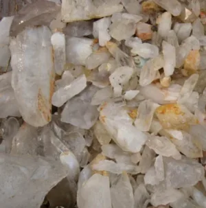 Närbild på Bergkristall rund ädelsten 4-6mm, med grova, opolerade klara kvartskristaller med gulaktiga och brunaktiga mineralfläckar i olika storlekar och oregelbundna former grupperade tillsammans.