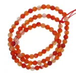 En slingrad tråd av Karneol rund ädelsten 4-6mm, med runda orange och röda genomskinliga pärlor trädda på en synlig röd tråd.
