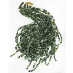 Flera trådar av Mossagat rund ädelsten 4-8mm gröna pärlor är löst sammanlindade mot en vit bakgrund, med några lösa trådar synliga i ändarna.