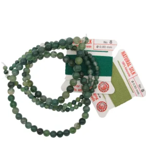En tråd med Mossagat rund ädelsten 4-8 mm gröna pärlor visas bredvid två kort med grön natursilketråd, var och en märkt storlek 8 (0,80 mm), arrangerade på en vit bakgrund.