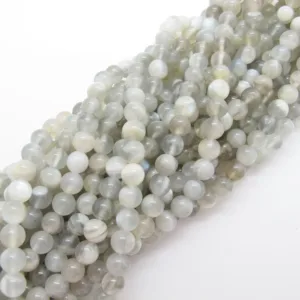 Närbild av flera trådar av Månsten rund ädelsten 6mm, med släta och blanka runda grå och vita pärlor, löst placerade mot en vit bakgrund.