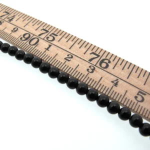 En trälinjal markerad i tum och centimeter ligger ovanför en rad små, runda, glänsande svarta pärlor som är arrangerade i en rak linje mot en vit bakgrund.