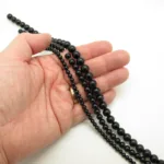 En hand håller i tre trådar med runda svarta pärlor i olika storlekar mot en vit bakgrund.