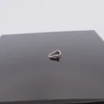 Trekantsögla slät i sterlingsilver, en liten silvermetallring med oregelbunden form, vilar på en blank svart kvadratisk yta mot en slät ljus bakgrund.