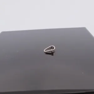 Trekantsögla slät i sterlingsilver, en liten silvermetallring med oregelbunden form, vilar på en blank svart kvadratisk yta mot en slät ljus bakgrund.