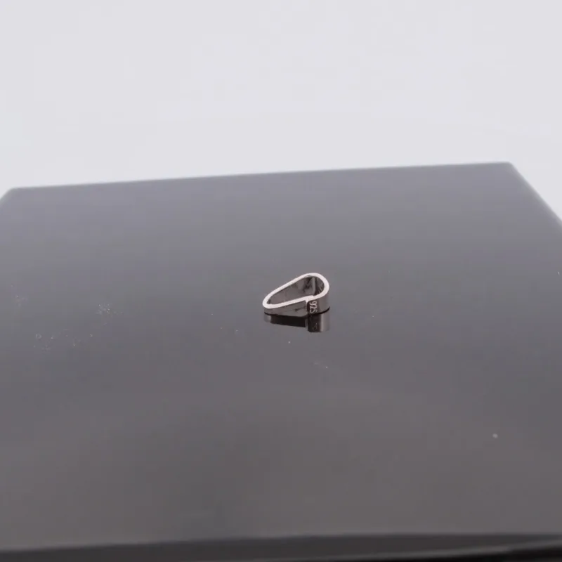 Trekantsögla slät i sterlingsilver, en liten silvermetallring med oregelbunden form, vilar på en blank svart kvadratisk yta mot en slät ljus bakgrund.