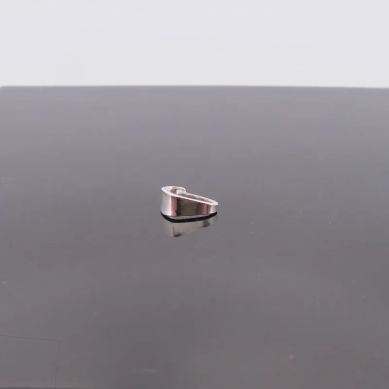 A Trekantsögla slät i sterlingsilver, ett litet, kilformat föremål i sterlingsilver, är centrerat på en reflekterande mörk yta med en vanlig ljus bakgrund.
