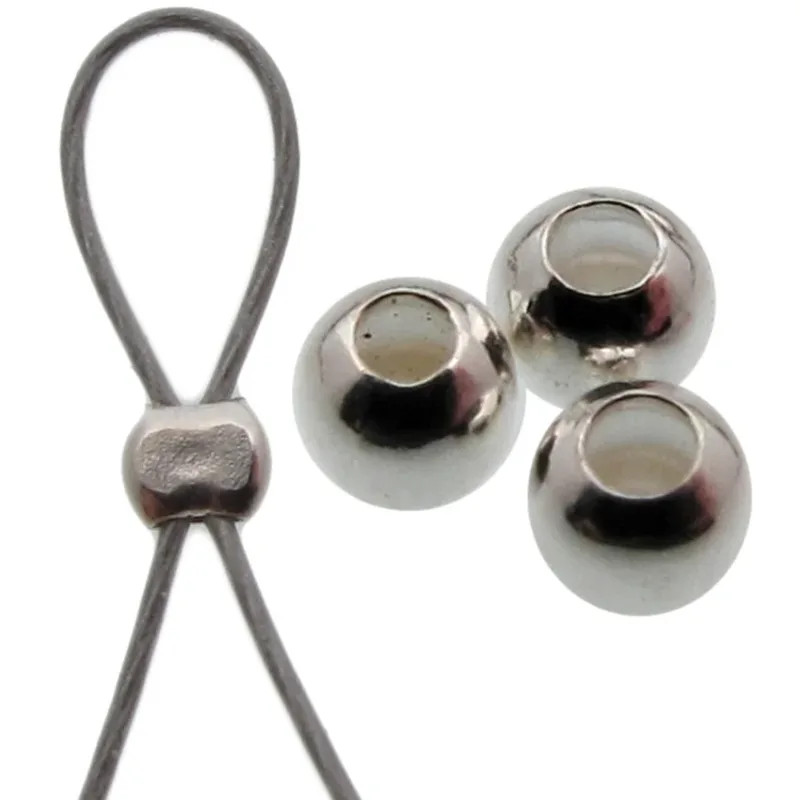 Närbild av en Klämpärla i sterlingsilver 1,8 mm som fäster i en trådögla, bredvid tre lösa blanka runda silverpärlor med stora hål, mot en vit bakgrund.