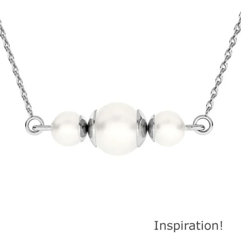 Ett silverkedjehalsband med tre vita Pärlhatt Sterlingsilver 6mm pärlor i mitten, accentuerat av små silverdetaljer. "Inspiration!" visas i det nedre högra hörnet.