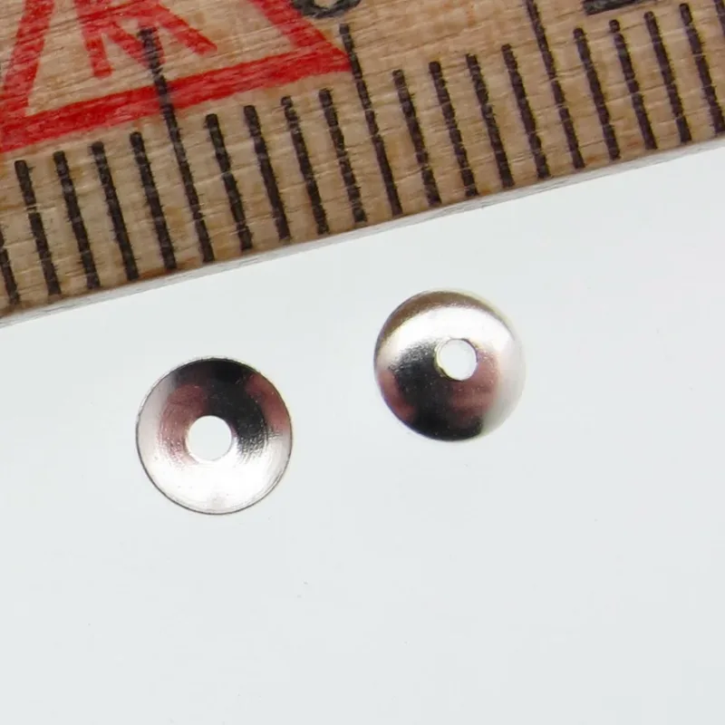 Två 4 mm pärlhattar av sterlingsilver från Pärlhatt med centrala hål är placerade på en vit yta bredvid en trälinjal markerad med röda och svarta måttlinjer.