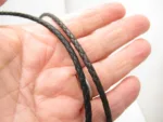 Närbild av en hand som håller i två tunna, svarta flätade lädersnören mot en ljus bakgrund.