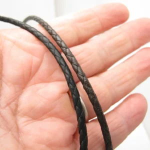 Närbild av en hand som håller i två tunna, svarta flätade lädersnören mot en ljus bakgrund.