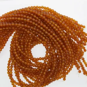 Flera trådar med små, runda, orange pärlor är lindade i ett löst spiralmönster mot en vit bakgrund. Pärlorna har ett glänsande, genomskinligt utseende.