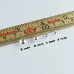 En uppsättning Silverpärlor runda blanka 4mm/1,2mm pärlor visas uppradade efter storlek bredvid en trälinjal markerad i centimeter och millimeter.