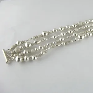 Silverpärlor runda blanka 4mm/1,2mm armbandet har flera strängar av glänsande runda silverpärlor i olika storlekar och texturer, säkrade med ett bar och toggle lås, visat på en vit bakgrund.