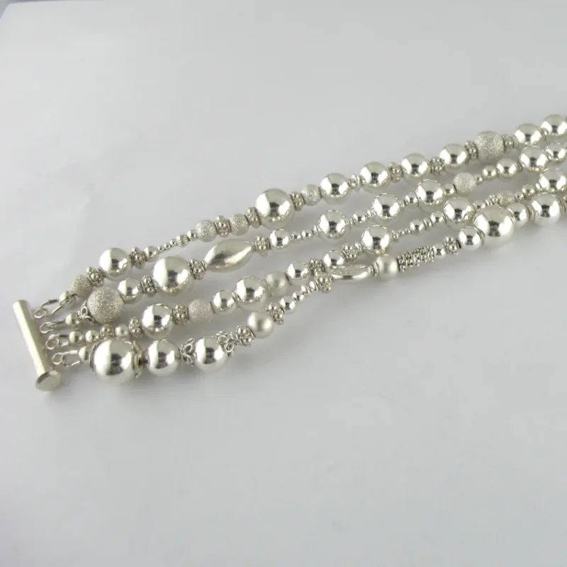 Silverpärlor runda blanka 4mm/1,2mm armbandet har flera strängar av glänsande runda silverpärlor i olika storlekar och texturer, säkrade med ett bar och toggle lås, visat på en vit bakgrund.