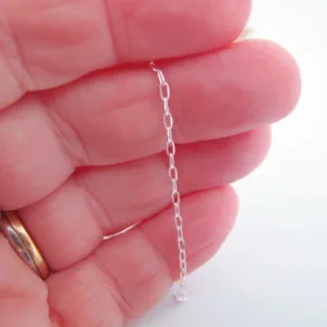 En hand med en guldring håller i Oval kabelkedja i sterlingsilver - 10cm, en delikat kedja i sterlingsilver med långsträckta ovala länkar, mot en vit bakgrund.