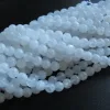 Närbild av flera trådar av Månsten Vit rund ädelsten 6mm pärlor, runda och genomskinligt vita, arrangerade på en mörk yta.