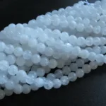 Närbild av flera trådar av Månsten Vit rund ädelsten 6mm pärlor, runda och genomskinligt vita, arrangerade på en mörk yta.