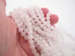 Närbild av en hand som håller i flera trådar av Månsten Vit rund ädelsten 6mm pärlor, med sitt runda, genomskinliga vita utseende mot en vit bakgrund.