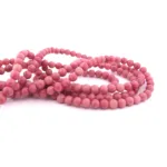 Närbild av flera trådar av Rodonit rund smyckesten 4-6 mm, polerade rosa pärlor, löst lindade mot en vit bakgrund.