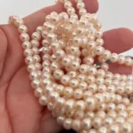 En hand håller i flera strängar av Odlad sötvattenpärla creme 6mm-glänsande, runda, krämfärgade sötvattenpärlor med mjuk lyster.