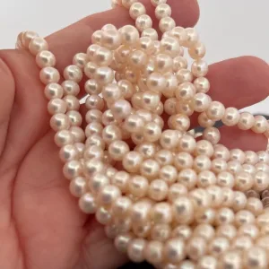En hand håller i flera strängar av Odlad sötvattenpärla creme 6mm-glänsande, runda, krämfärgade sötvattenpärlor med mjuk lyster.