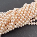 Närbild på Odlad sötvattenpärla creme 6mm, med flera runda, ljusrosa sötvattenpärlor arrangerade tillsammans på en mörk, strukturerad yta.