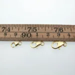 En karbinhake i förgyllt sterlingsilver 5x8mm visas under en trälinjal på en vit bakgrund, med längden tydligt markerad.