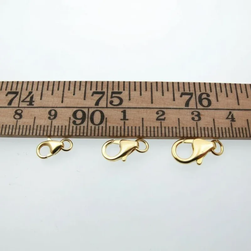 En karbinhake i förgyllt sterlingsilver 5x8mm visas under en trälinjal på en vit bakgrund, med längden tydligt markerad.