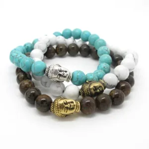 Tre pärlarmband med Buddhahuvudberlocker: ett med turkosa pärlor och en Buddha i silver, ett med vita pärlor och en Buddha i silver samt ett med bruna pärlor och två Buddhahuvuden i guld, alla i en lös stapel.