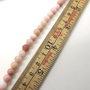 Ett pärlband med små runda rosa och persikofärgade pärlor placeras bredvid en trälinjal, vilket visar att pärlorna är ca 8 mm i diameter.