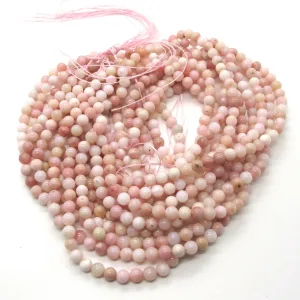 Flera trådar med runda, ljusrosa pärlor är löst hoprullade på en vit yta, med rosa tråd som knyter ihop ändarna på varje tråd.