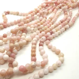 Flera trådar med runda, polerade pärlor i mjuka nyanser av rosa, persika och grädde är utlagda på en vit yta. Pärlorna är blanka och enhetliga i storlek, vilket skapar ett delikat och elegant utseende.