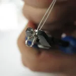 En närbild visar en hand som använder en tång för att fästa en Krympkåpa sterlingsilver 3mm på två tunna trådar, troligen vid smyckestillverkning. Den suddiga bakgrunden drar uppmärksamheten till spännet och tången i fokus.