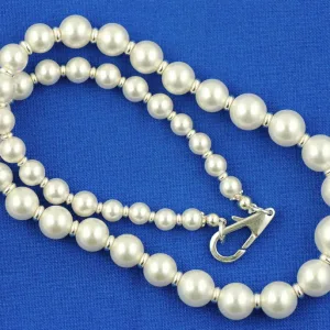 Krympkåpa halsband i sterlingsilver, 3 mm, med vita pärlor, silverfärgade distanspärlor och stort silverfärgat karbinlås, på ljusblått tyg.