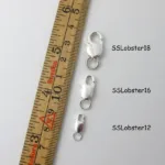 Tre Silverlås karbinhake avlång spännen (12mm, 16mm, 18mm) visas bredvid en centimeter linjal för skala.