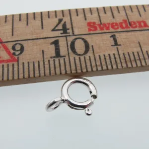 En Ringlås sterlingsilver - öppen ögla 7mm visas nedanför en trälinjal märkt Sverige, som visar centimetermått. Det lilla fjäderringlåset i silver mäter ca 7 mm i diameter.