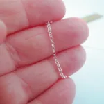 En hand håller i Silverkedja ärtlänk YD 1,8 mm - 10 cm och visar dess fina cirkelformade länkar i detalj med en suddig linjal i bakgrunden.