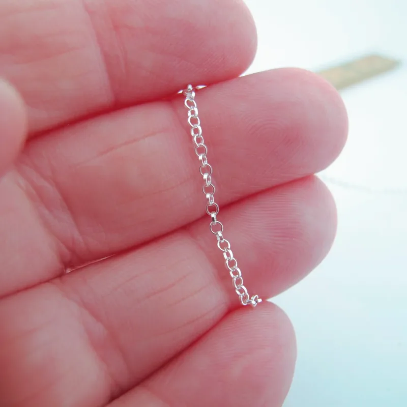 En hand håller i Silverkedja ärtlänk YD 1,8 mm - 10 cm och visar dess fina cirkelformade länkar i detalj med en suddig linjal i bakgrunden.