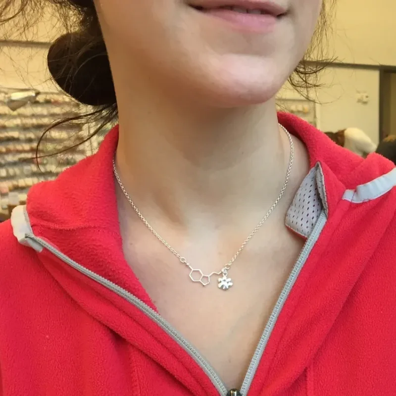 En person iklädd en röd jacka med dragkedja och ett Silverkedja ärtlänk YD 1,8mm - 10cm halsband med ett hänge i form av en kemisk struktur och en liten snöflinga som berlock.