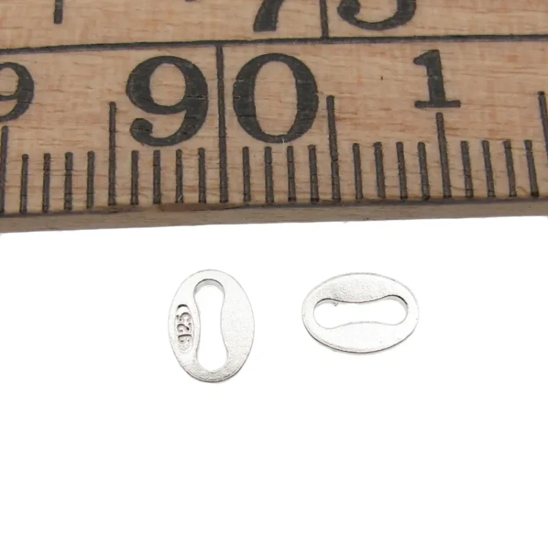 Två Hallmark kvalitetslänkspännen, ca 4x5mm och ovala, visas under en trälinjal för skala. Varje silverspänne har ett mittfack och är stämplat "925" för att indikera sterling silverkvalitet.